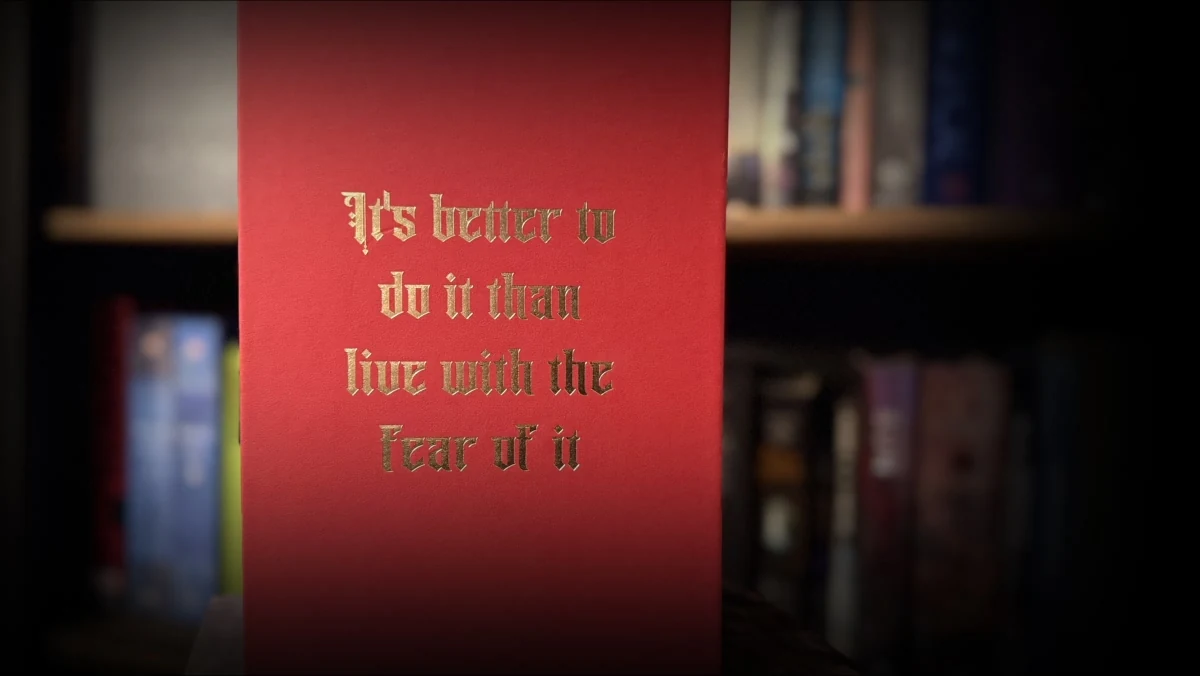 A panel of the red First Law slipcase stamped in gold blackletter type with the quote, It is better to do it than live with the fear of it.