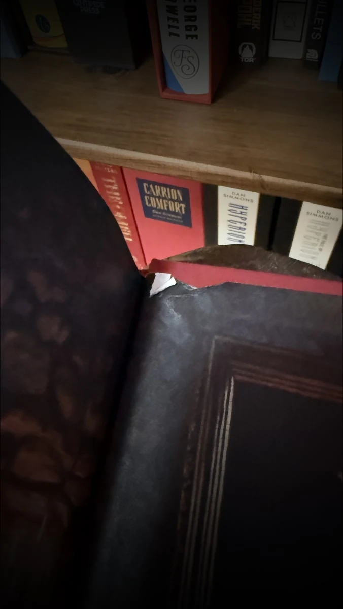 The Last Argument of Kings hardcover held open, with the endpaper torn away along the gutter so the red board and the white paper edge show through the gap.