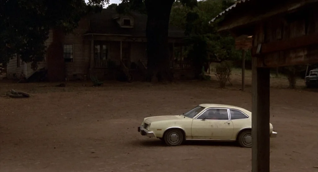 A white Ford Pinto parked alone in the dusty dooryard of the Camber farmhouse in the 1983 film Cujo.
